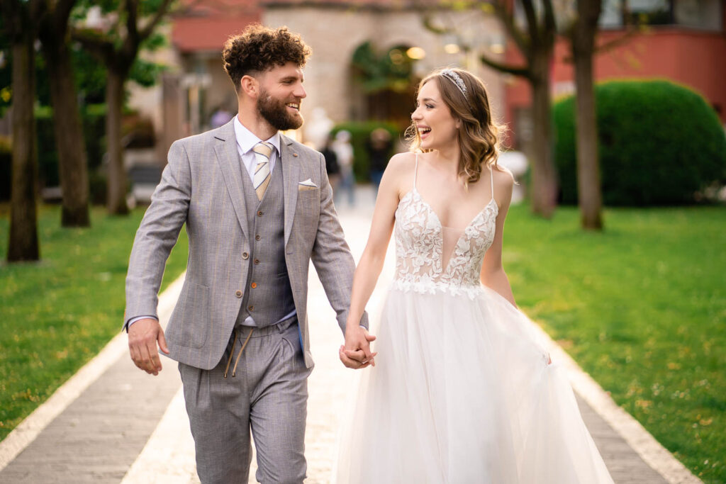Wunderschöne Braut und Ehemann lachen in einem langen Kleid in Sirmione, Italien. Hochzeitsfotograf