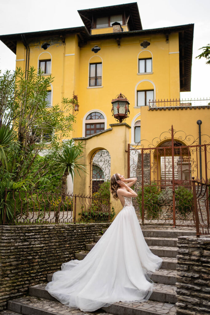 Elegante Braut in einem langen Kleid vor einer großen Villa in Sirmione, Italien. Hochzeitsfotograf
