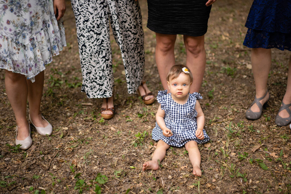 Ein kleines Mädchen sitzt bei der Hochzeit zu Füßen der Erwachsenen auf dem Boden. Ein besonderer künstlerischer Plan. Hochzeitsfotograf Wien