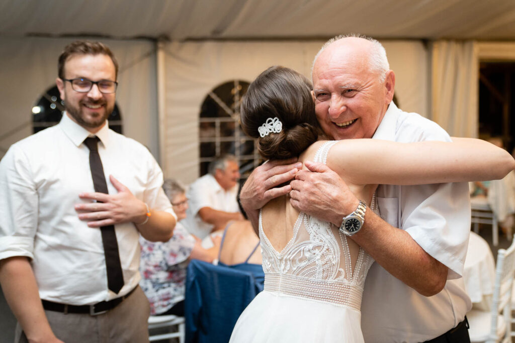 Der Großvater lächelt und umarmt die Braut bei der Hochzeit. Ein besonderer Moment, für den es sich lohnt, einen professionellen Fotografen anzurufen. Hochzeitsfotograf Wien