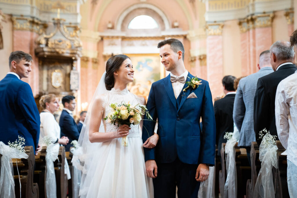 Verlassen der Kirche nach der Hochzeit. Braut und Bräutigam lächeln einander an. Ein besonderer Moment. Hochzeitsfotograf Wien