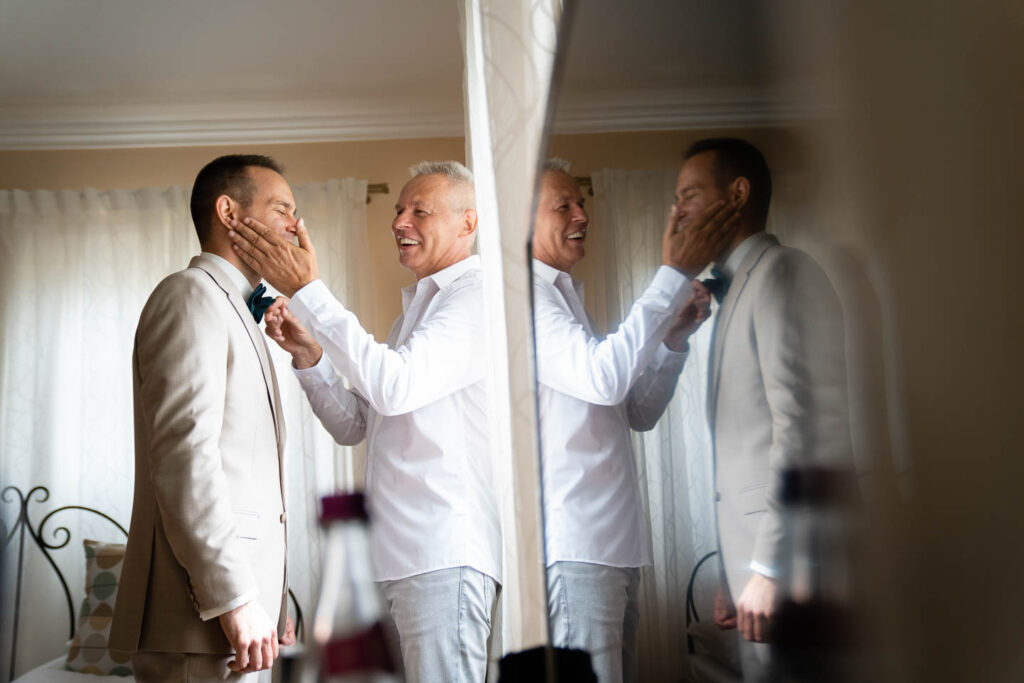 Der Bräutigam wird bei der Hochzeit von seinem Vater eingekleidet. Besonderes künstlerisches Foto mit Reflexion. Hochzeitsfotograf Wien