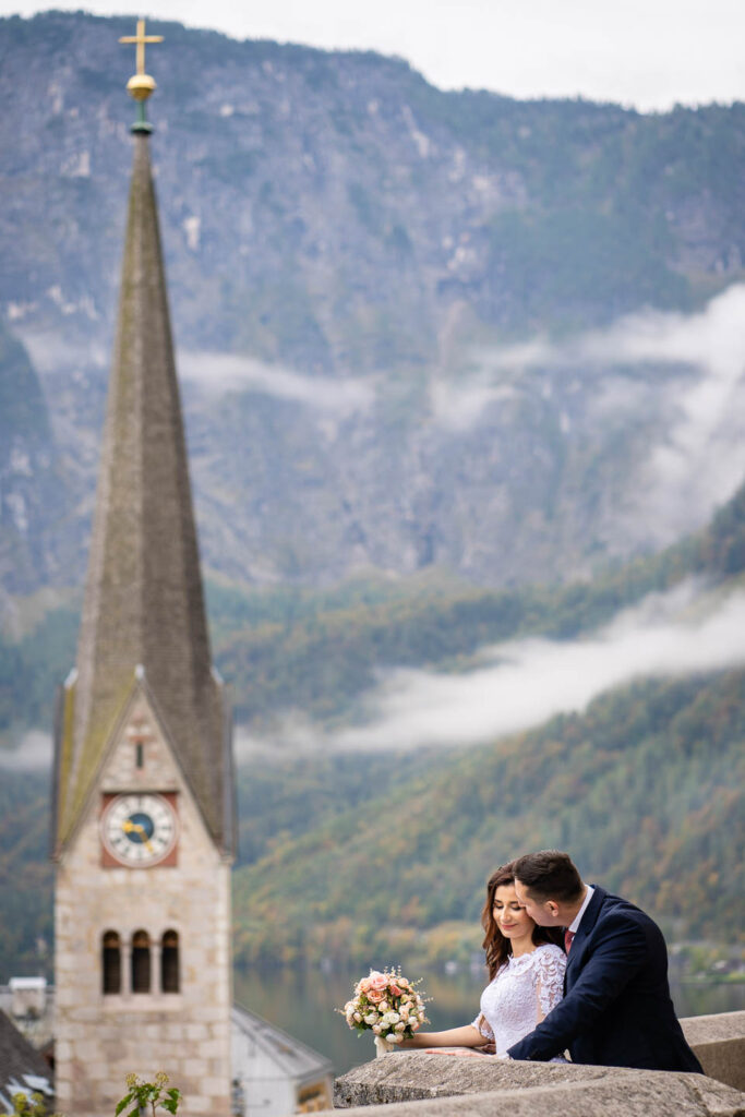 Hochzeitspaar in Hallstatt mit einer Kirche im Hintergrund. Professioneller Hochzeitsfotograf Wien