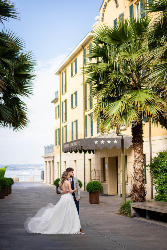 Elegantes Hochzeitspaar unter Palmen vor einem Hotel in Sirmione. Professioneller Hochzeitsfotograf Wien