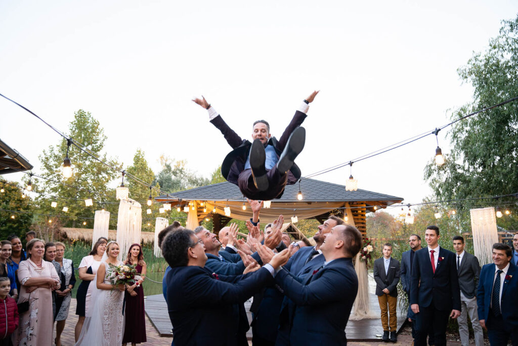 Der Bräutigam wird bei der Hochzeit von seinen Freunden in die Luft geworfen. Extremes Hochzeitsfoto. Hochzeitsfotograf Wien