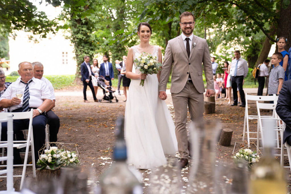 Ein lächelndes Hochzeitspaar kommt zur Ihre Zeremonie in einen Wald. Professioneller Hochzeitsfotograf Wien